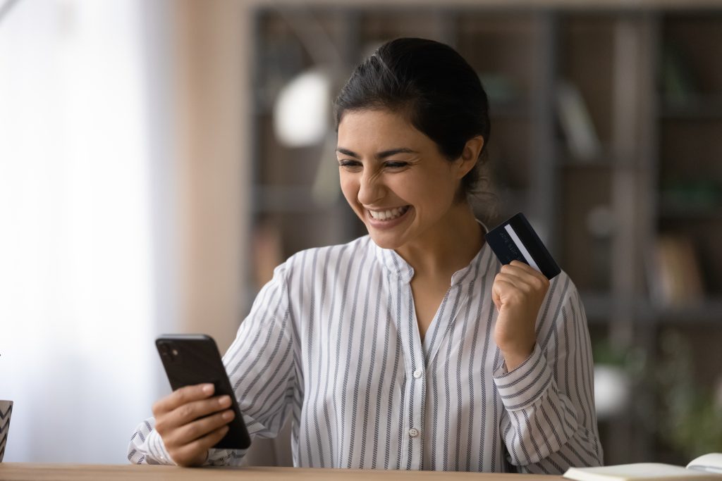 Mulher sorridente com cartão de crédito na mão e smartphone, simbolizando como atrair o público certo por ofertas estratégicas.