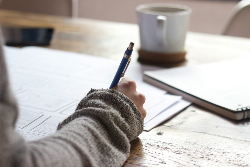 Pessoa escrevendo checklist do processo de onboarding à mão sobre a mesa